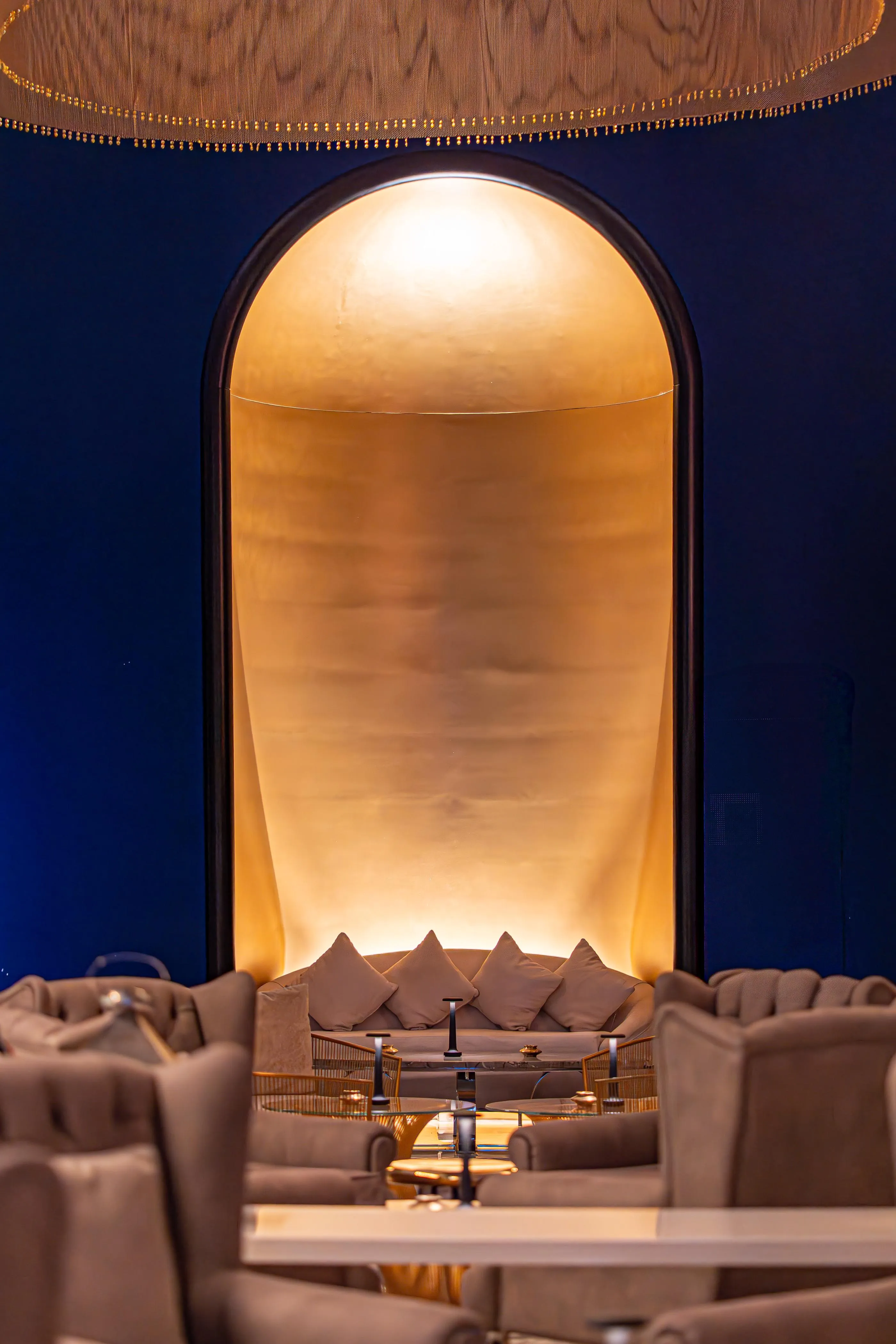 Un espacio interior con sofás y una mesa baja, iluminado por una luz dorada a través de un arco.