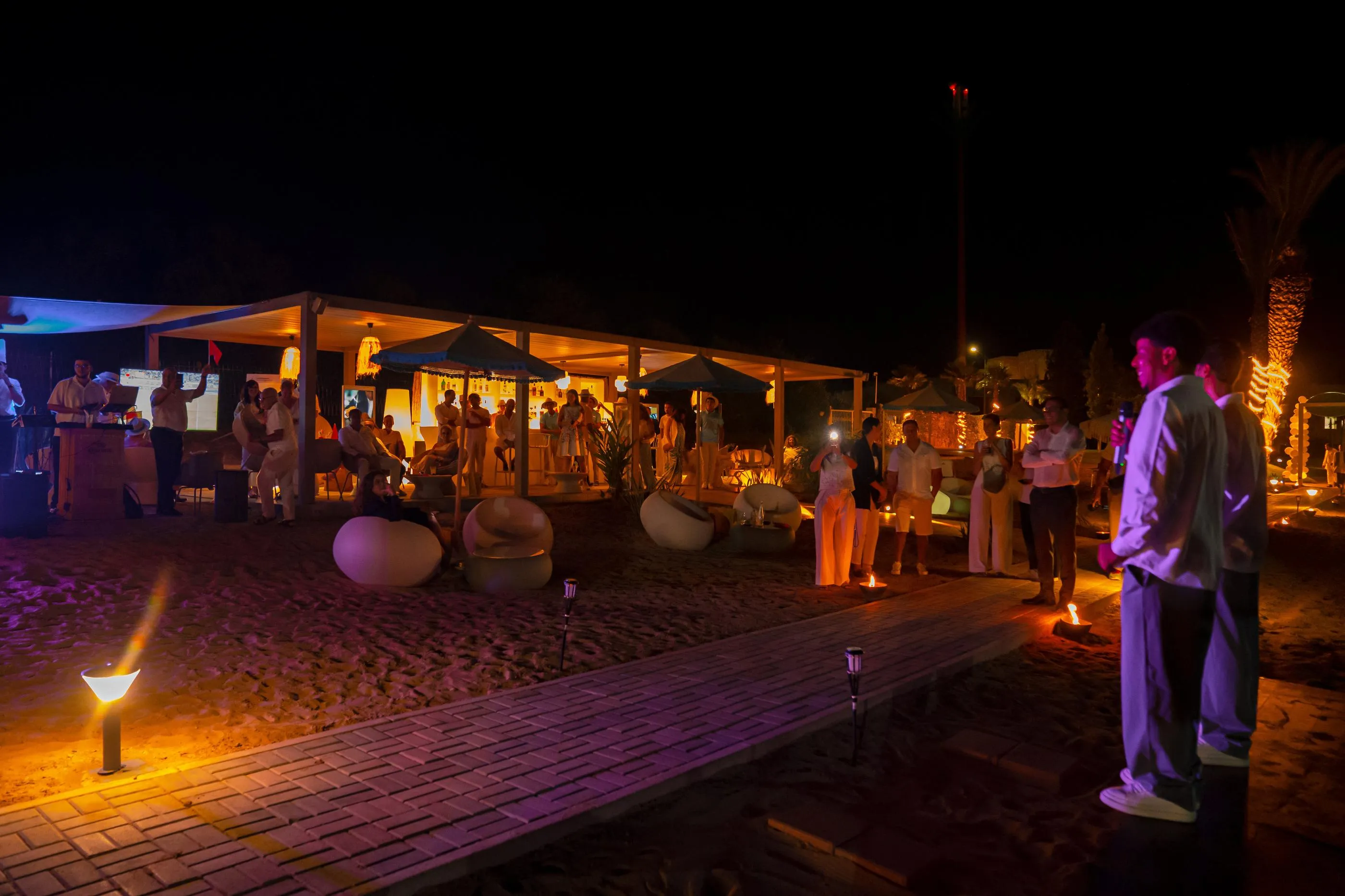 Un grupo de personas se congrega alrededor de una estructura iluminada en una playa de noche