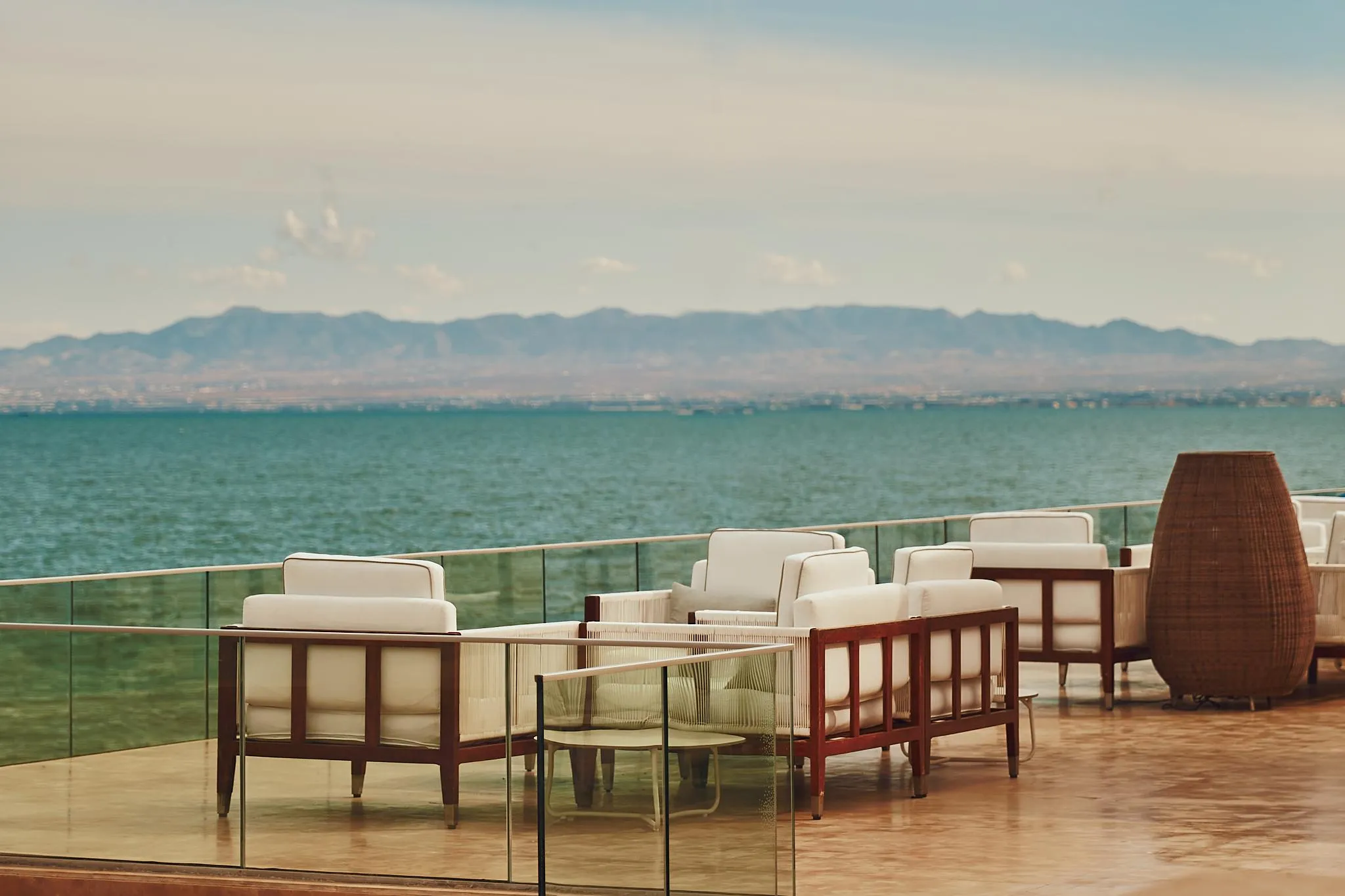 Terraza con sillas y mesas frente a un mar y montañas en el horizonte
