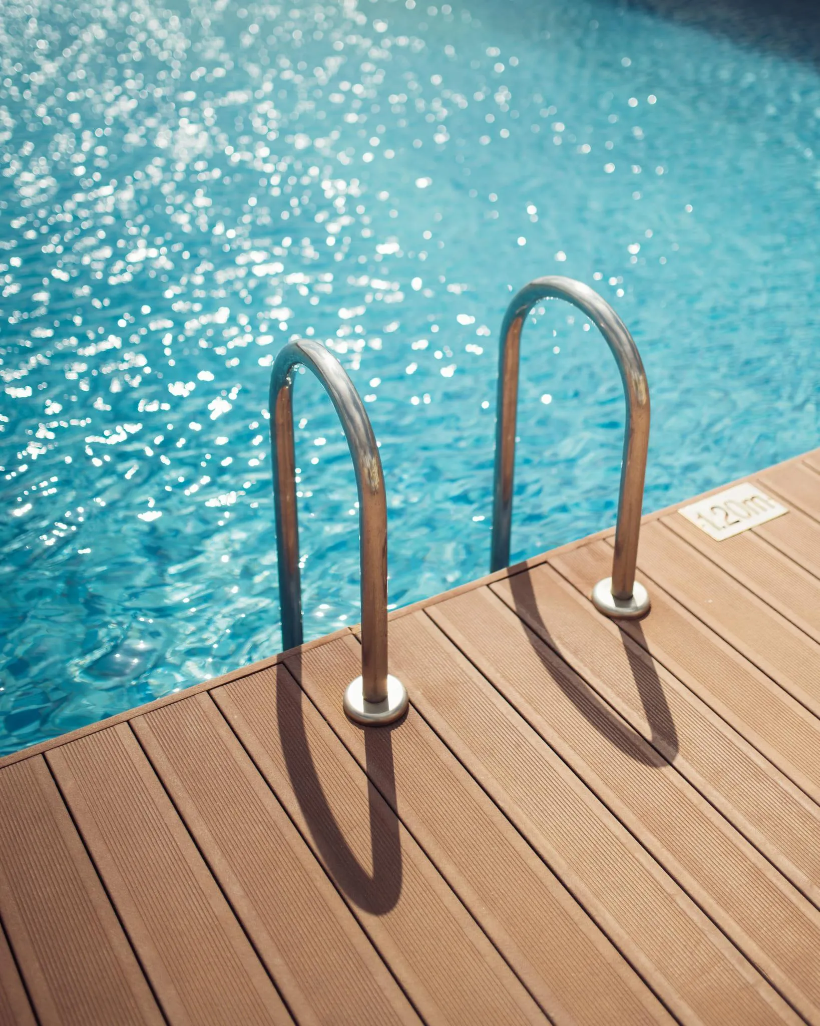 Dos barras metálicas curvadas fijadas a un suelo de madera cerca de una piscina llena de agua azul