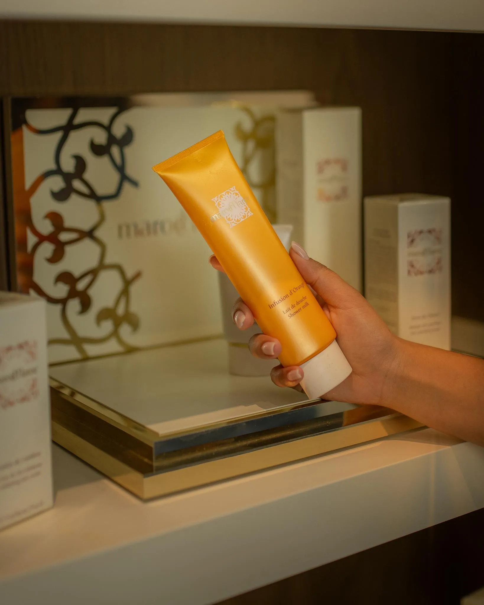 Une main tient un tube de produit cosmétique devant une étagère avec d'autres produits