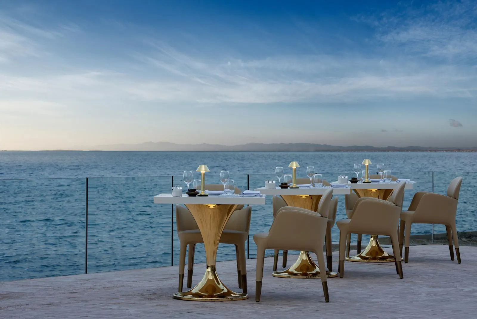 Tables et chaises disposées sur une terrasse face à la mer avec des verres et des serviettes, sous un ciel dégagé