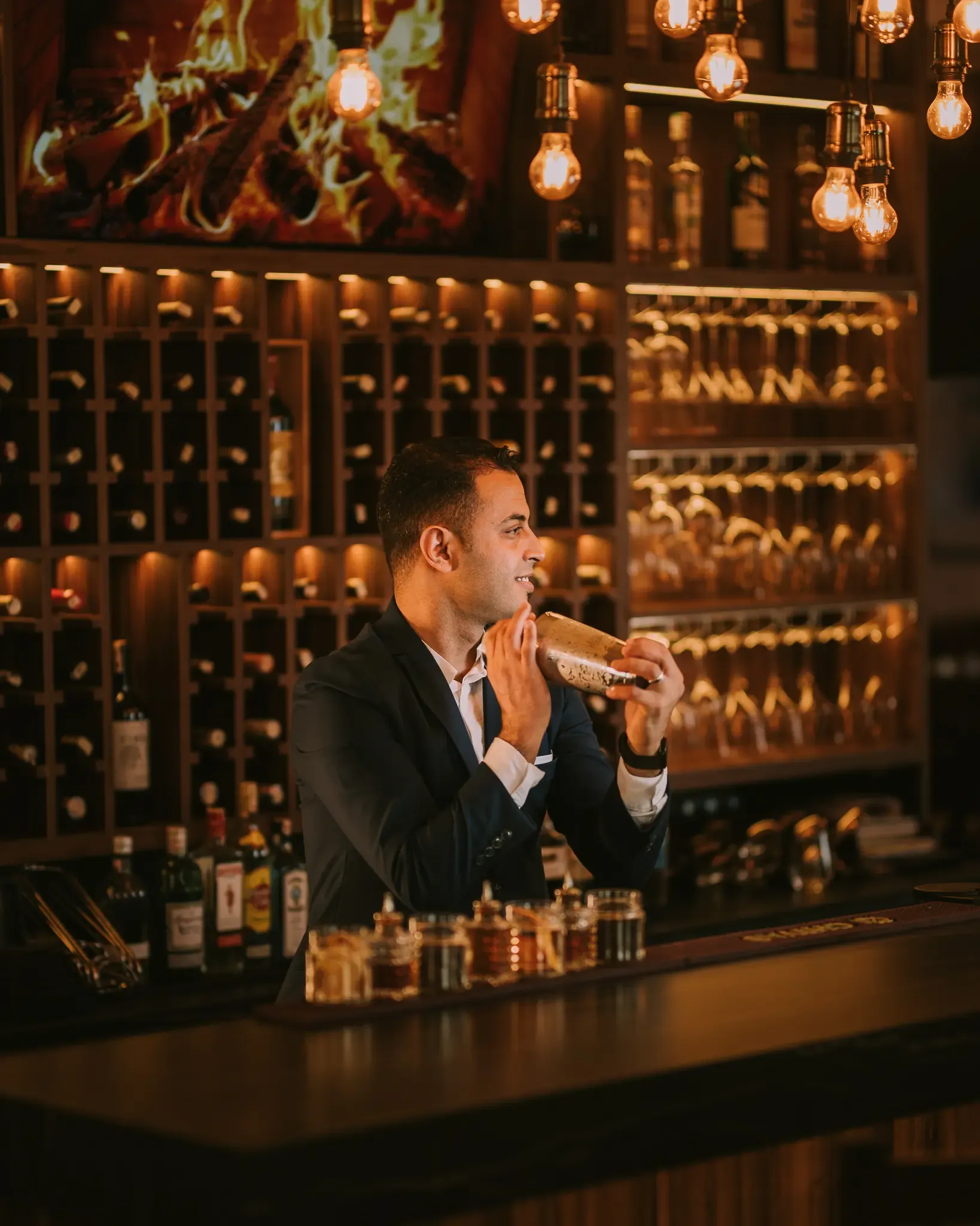 Un homme en costume mange un sandwich derrière un bar bien éclairé avec des bouteilles et des verres