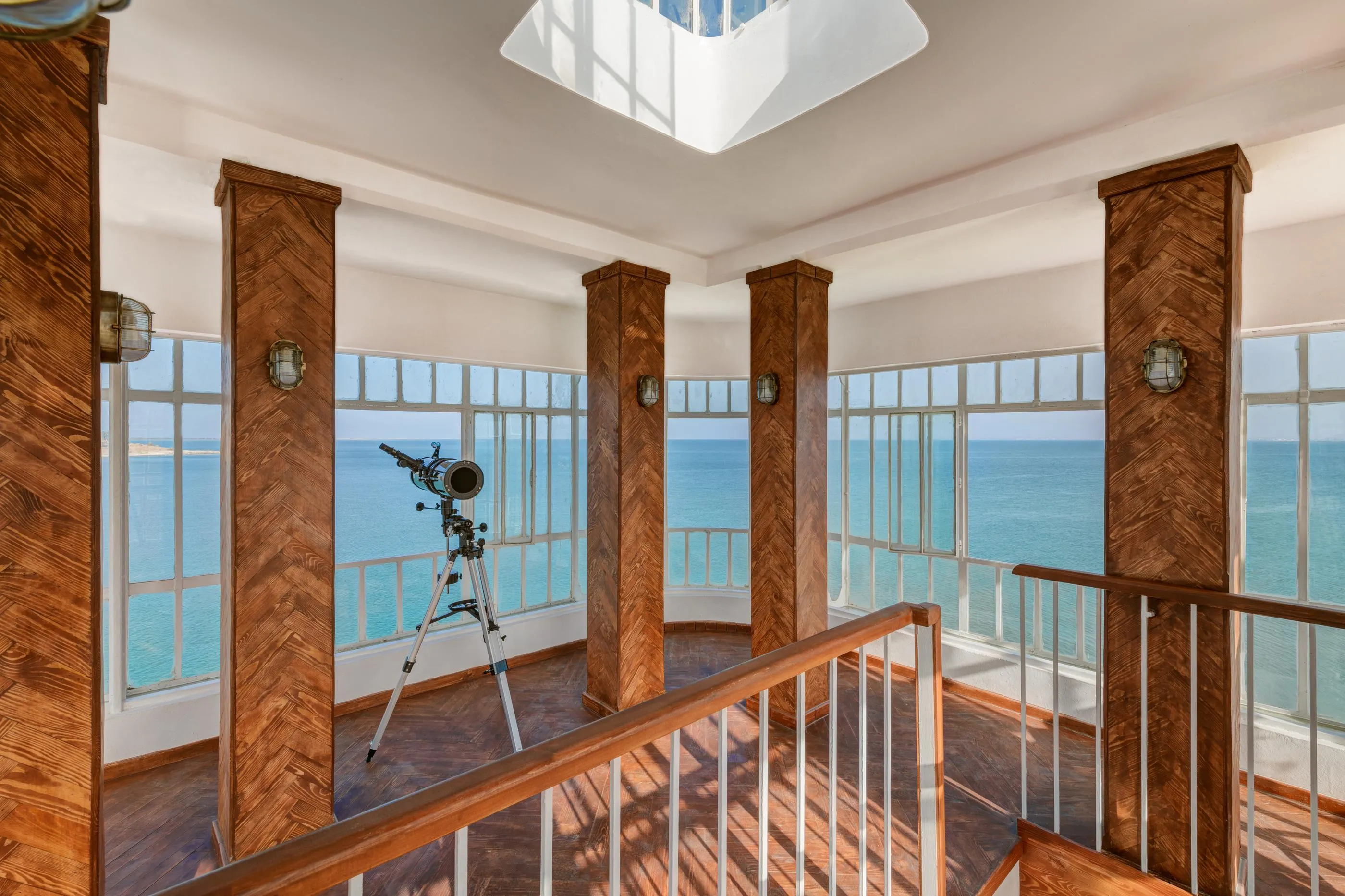 A telescope is installed on a wooden balcony with a sea view.