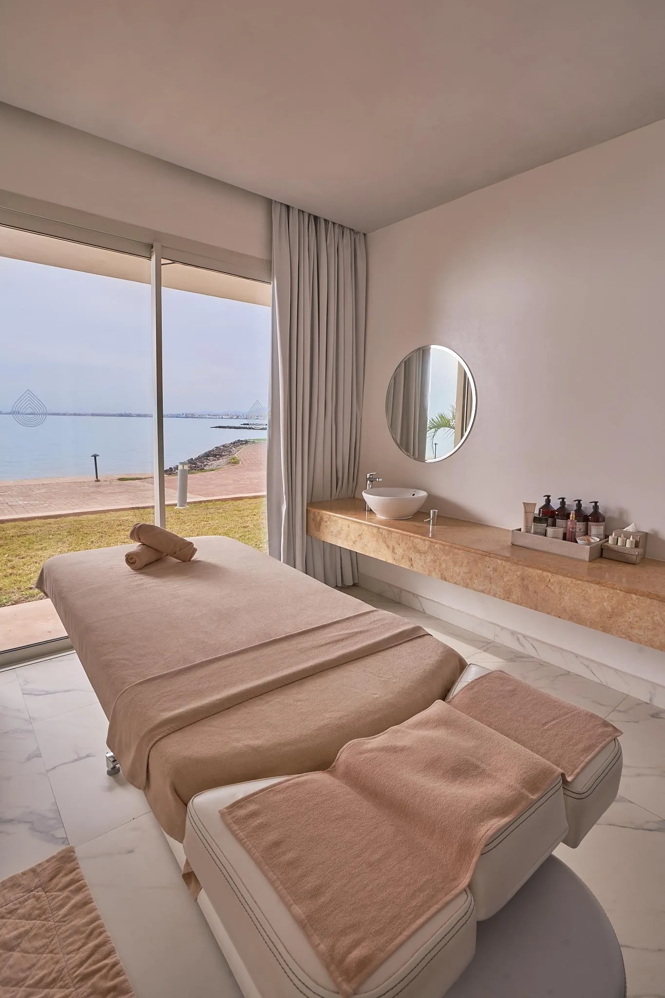 Sala de masajes con dos mesas de tratamiento, un lavabo y vista al mar
