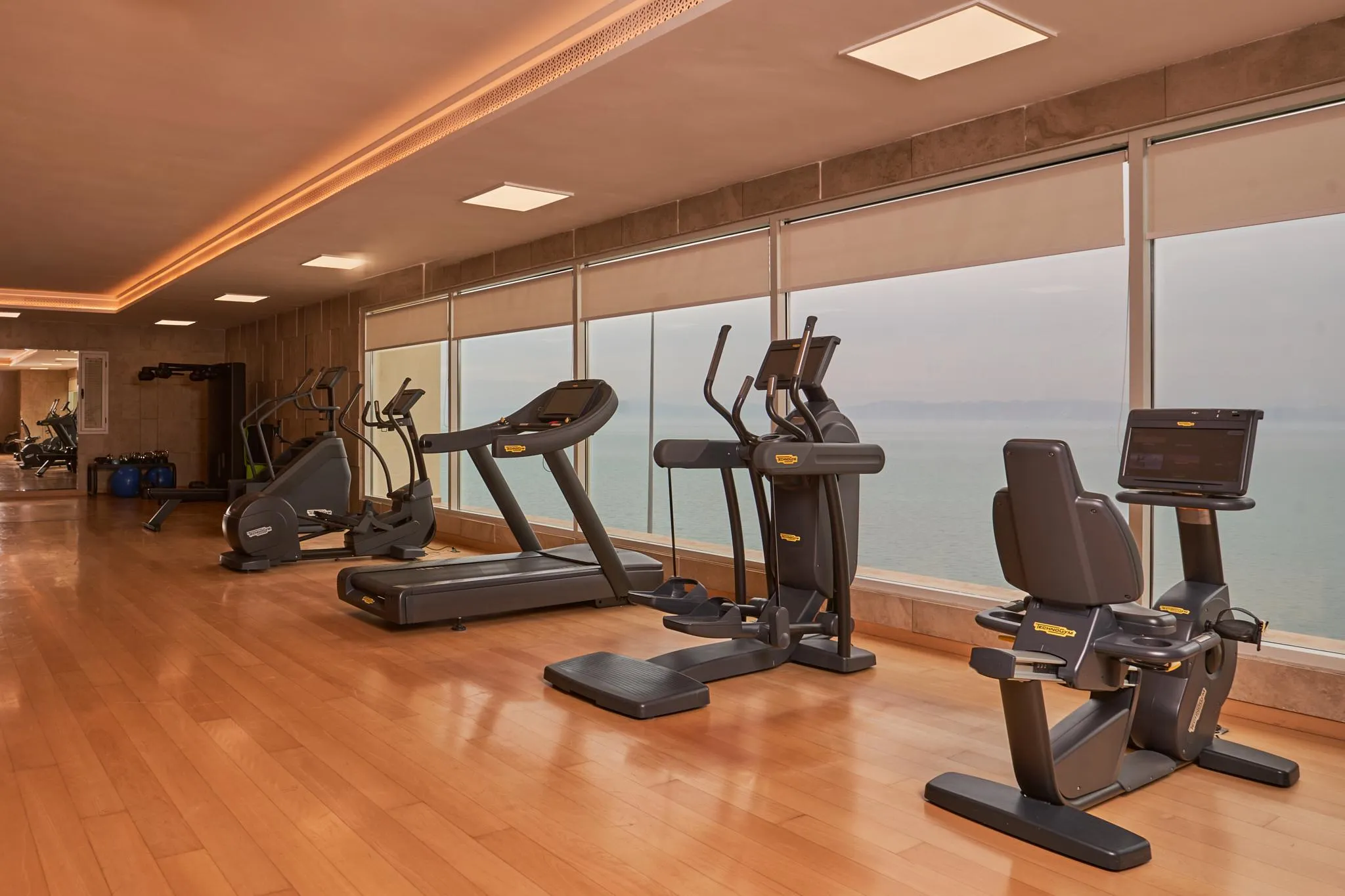 Sala de deportes con varios aparatos de fitness frente a una gran ventana que ofrece vistas al mar