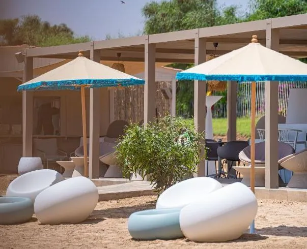 Un espacio exterior con sofás blancos y azules, sombrillas con flecos azules y pérgolas de madera