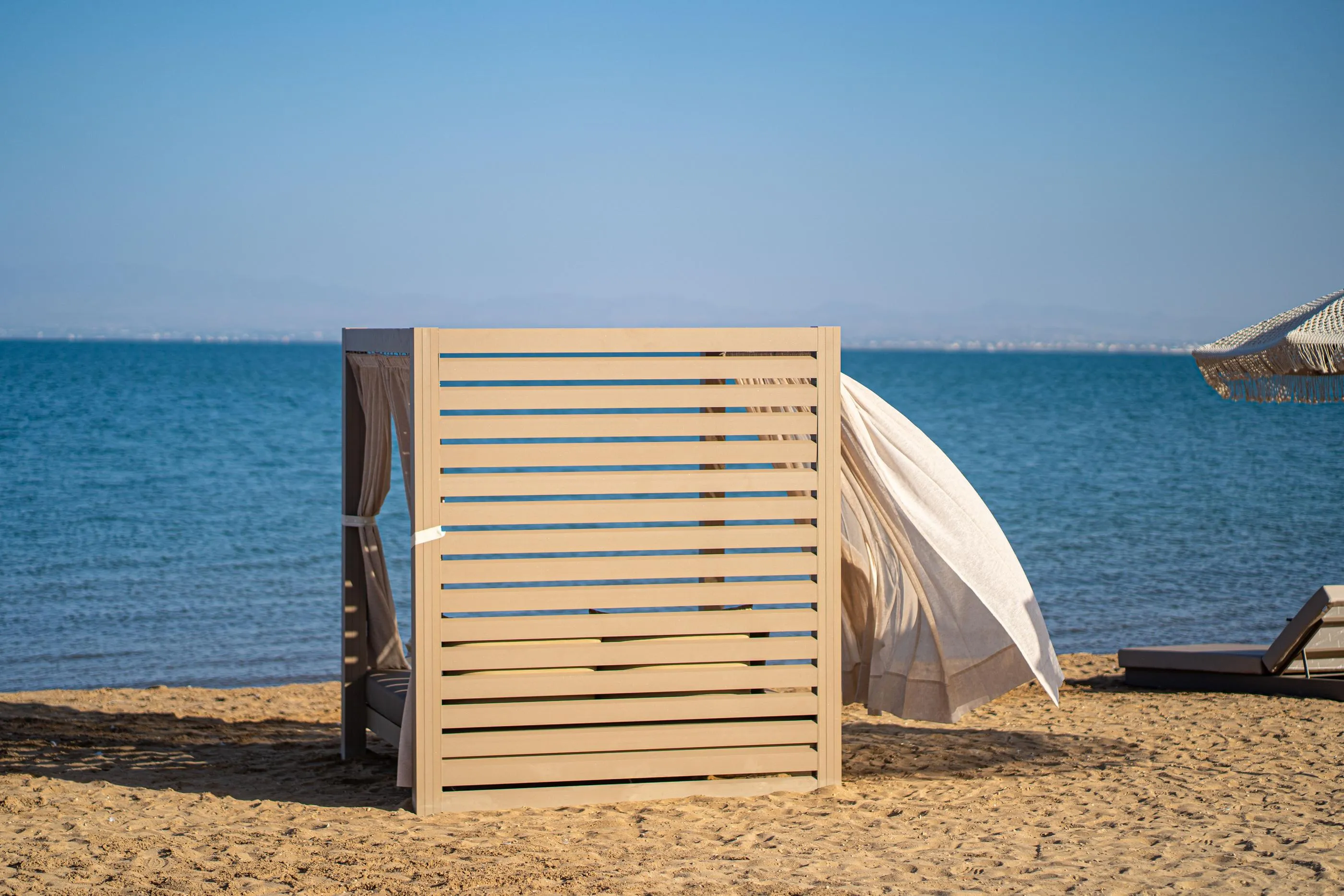 Cabaña de madera en una playa de arena con una lona blanca y vista al mar azul