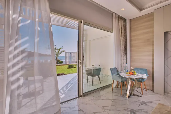 Una mesa con frutas y vasos está instalada cerca de una puerta de cristal abierta a un balcón con vistas al mar