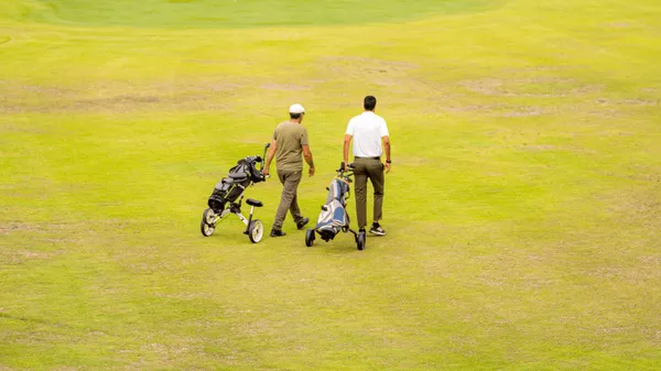 Dos personas caminan por un campo de golf empujando carritos de palos.