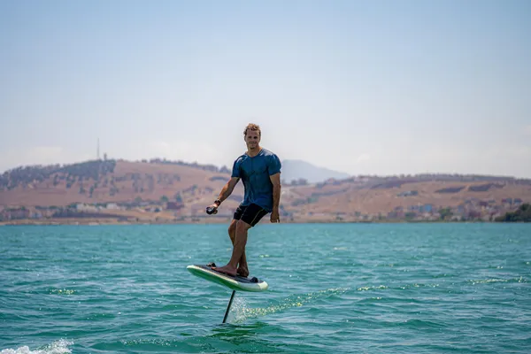 A man standing on a paddleboard in a body of water with hills in the background.