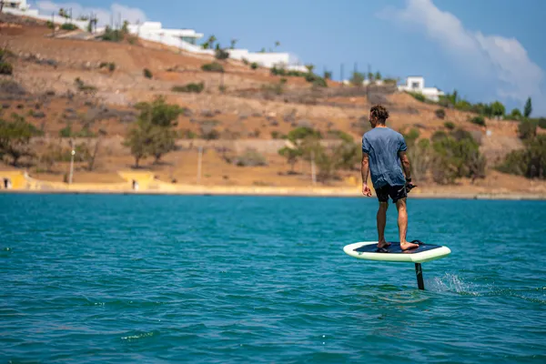 Un homme debout sur une planche de paddle électrique sur une étendue d'eau avec un paysage aride en arrière-plan
