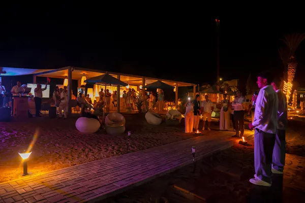 Un grupo de personas se congrega alrededor de una estructura iluminada en una playa de noche