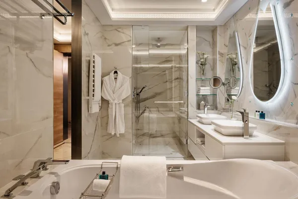 Salle de bain luxueuse avec baignoire, douche en verre, double vasque et miroir rond éclairé